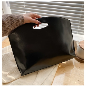 Minimalist large black leather handbag with unique oval cutout handle shown in office setting