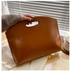 Close-up of brown leather handbag featuring a unique oval cutout handle and clean stitching