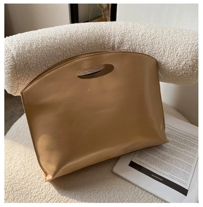 Close-up of caramel leather handbag with cutout handle on a cozy white armchair