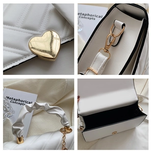 Detail view of white quilted handbag featuring gold heart buckle and ruched handle