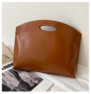 Detail view of a minimalist brown trapezoid handbag with a cut-out handle on textured fabric