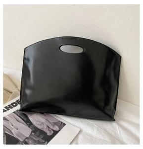 Minimalist black matte leather tote bag with cutout handle leaning on white wall