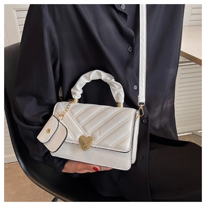 Detailed view of white quilted faux leather handbag with heart buckle and scrunchie handle