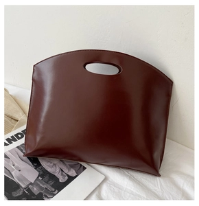 Detail of dark burgundy leather handbag with smooth finish and oval cutout handle
