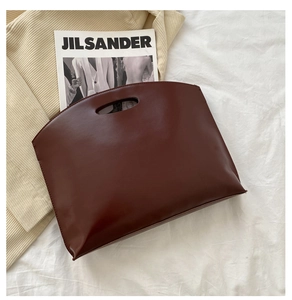 Flat lay of a minimalist deep burgundy leather tote bag with cut-out handle on white fabric