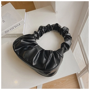 Draufsicht einer schwarzen Cloud Bag mit Falten auf minimalistischem Hintergrund mit Deko