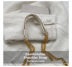 Détail de la bandoulière en cuir crème avec chaîne dorée sur une surface en tissu tweed