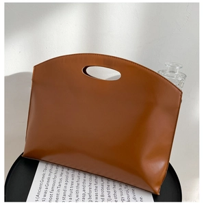 Detailed close-up of brown leather clutch bag with minimalist oval cutout handle design