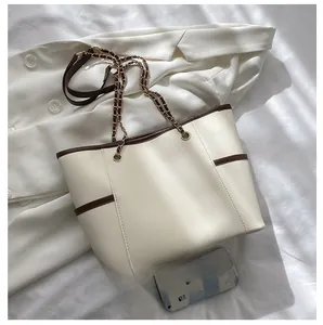 Detailed top view of large cream tote bag with chain strap compared with a phone size