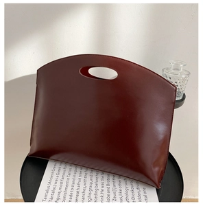 Detail of burgundy leather handbag with integrated circular cutout handle on side table