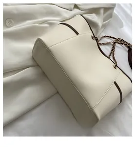 Detail view of the wide base and dark brown piping on this cream chain tote bag