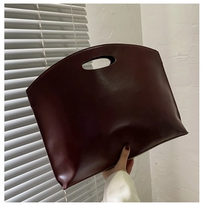 Close-up of dark burgundy matte leather tote bag with trapezoidal shape and cutout handle