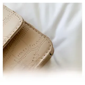 Detail shot of beige faux crocodile leather texture and precise stitching on a small bag
