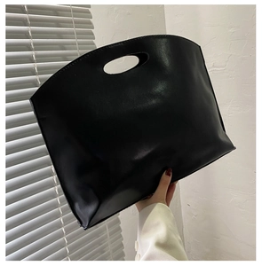 Detail of minimalist black matte leather handbag featuring an oval cutout handle design