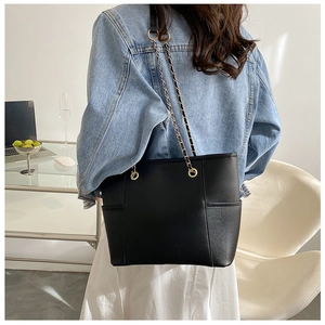 Close-up of black tote bag with gold chain straps and side pocket detail on a shoulder
