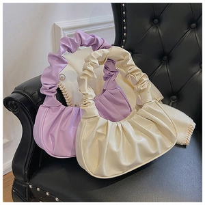 Nahaufnahme eleganter Falten-Cloud-Handtaschen in Lila und Creme auf einem Ledersofa