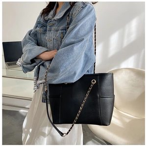 Side view of a black textured PU leather tote bag with elegant gold chain shoulder straps