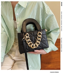 Detail of black quilted leather handbag with gold chunky chain and top handle