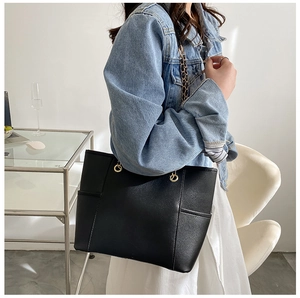 Close-up of a large black leather tote bag featuring gold chain straps and side pockets