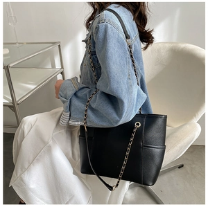 Detail of black leather tote bag featuring golden chain strap and side pocket design