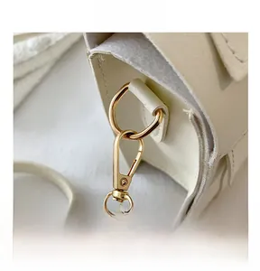 Detailed close-up of premium gold metal carabiner clip and fine stitching on cream leather bag