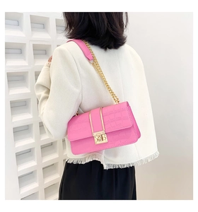 Detail of bright pink crocodile pattern crossbody bag with golden chain and square lock