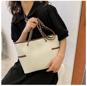 Detail of elegant cream tote bag with brown handles and stylish metal chain strap detail