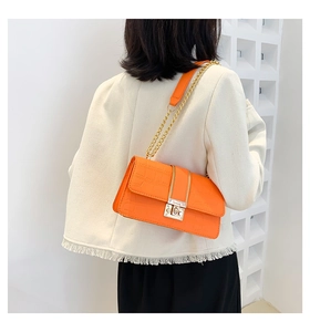 Rear view of model wearing an orange crocodile pattern crossbody bag with gold chain strap