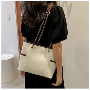Detail of cream tote bag with brown piping, litchi texture and chain strap on model