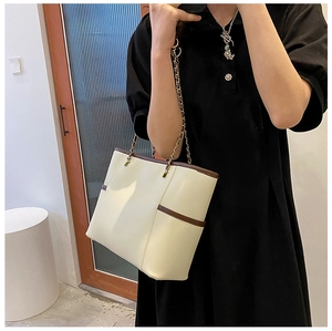 Detail of off-white tote bag with brown trim and gold chain strap worn by a model