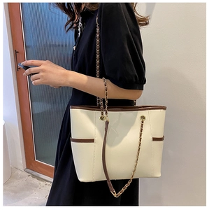 Detail of a chic cream tote bag with brown trim and gold chain shoulder strap