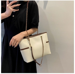 Detail of a chic cream tote bag with dark brown leather trim and golden chain strap