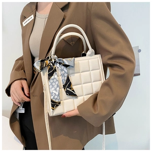 Détail du sac à main matelassé blanc avec foulard en soie sur un tailleur marron