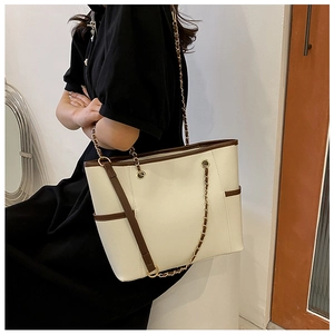 Detail of cream tote bag with brown trim and gold chain strap worn by a model