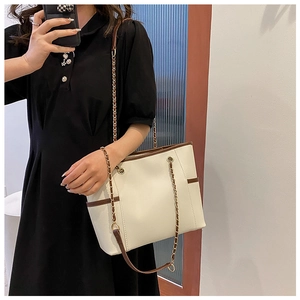 Detailed view of white leather tote bag with gold chain strap on black shirt dress