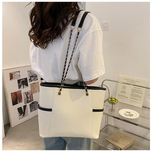 Macro detail of tote bag with black contrast piping and elegant metal chain strap