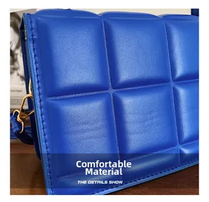 Detail of bright blue quilted handbag showing soft textured fabric and golden hardware hooks