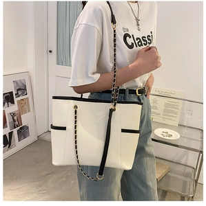 Detail of white tote bag featuring black contrast trim and metal chain shoulder strap