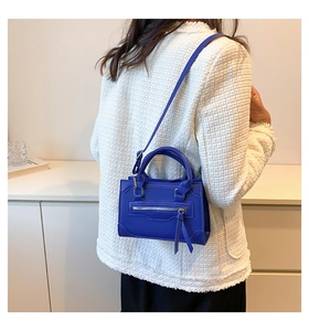 Detail of Klein blue crossbody bag with smiley face stitching on white tweed jacket