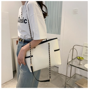 Detailed shot of white tote bag featuring woven chain strap and black contrast edging