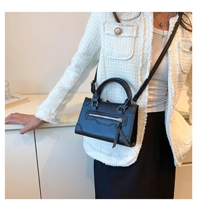 Detail view of black leather crossbody bag with metal zippers and long tassels on a model