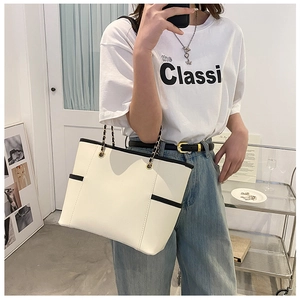 Detail of a creamy white tote bag with black edge piping and chain shoulder straps