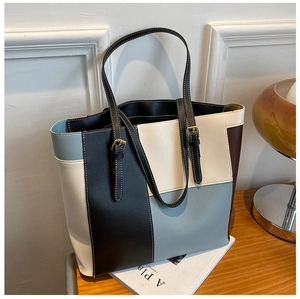 Detailed view of color-block tote bag with white contrast stitching and gold buckles