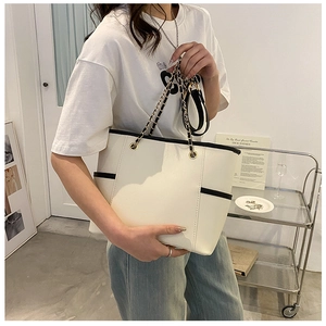 Side view of beige tote bag with black trim and chain strap worn by a model