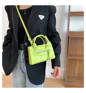 Neon green mini tote bag with fringe zipper detail worn over a stylish black blazer