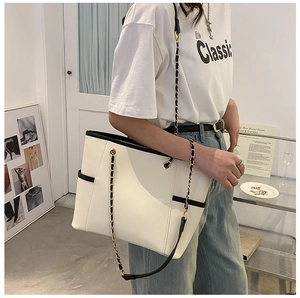Detail of a large cream tote bag with black contrast trim and metal chain shoulder strap