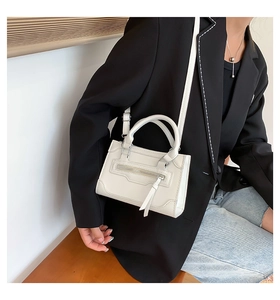 Detailed view of white leather crossbody bag featuring silver zippers and adjustable strap