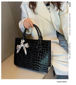 Detail of black crocodile texture handbag with decorative silk scarf and dual handles
