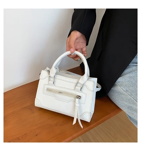 Detail of white PU leather handbag featuring silver zipper accents and smooth carry handle