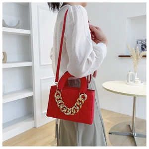Detail of red quilted handbag with bold gold chain strap shown on a model